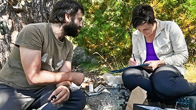 A researcher measures a bird while a participant records the data onto a clipboard (C) Caroline Dunn