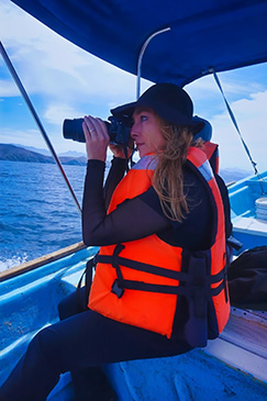 A woman on a motorboat looking through a camera for dolphins and whales