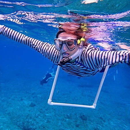 A woman snorkeling to a coral site with a transect around her body.