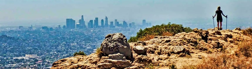 A woman on top of a rocky hill looking down on Los Angeles with visible air pollution.