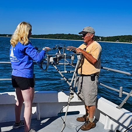 A girl and an older man on a boat preparing to toss scientific equipment overboard to conduct research.