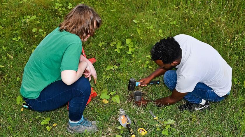 A man and a woman prepare a soil percolation test to help assess soil health.  