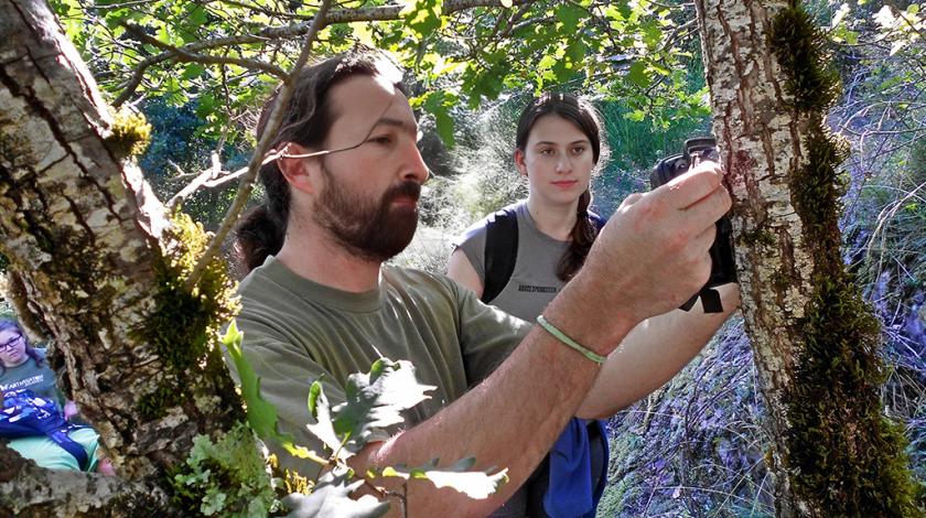 A researcher secures a camera trap on a tree trunk while a teen participant looks on (C) Amy Reggio